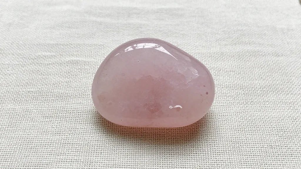 raw rose quartz palm stone on linen backdrop, diffused light