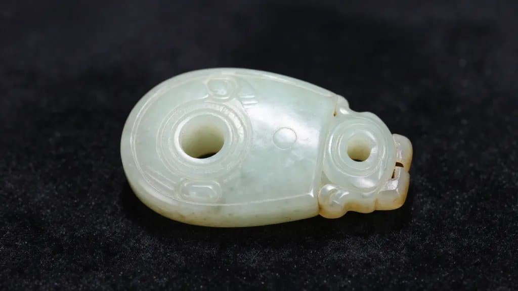 closeup of a solitary Mesoamerican jade ear spool on dark velvet
