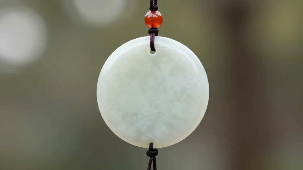 single jade stone wind chime disc against soft bokeh